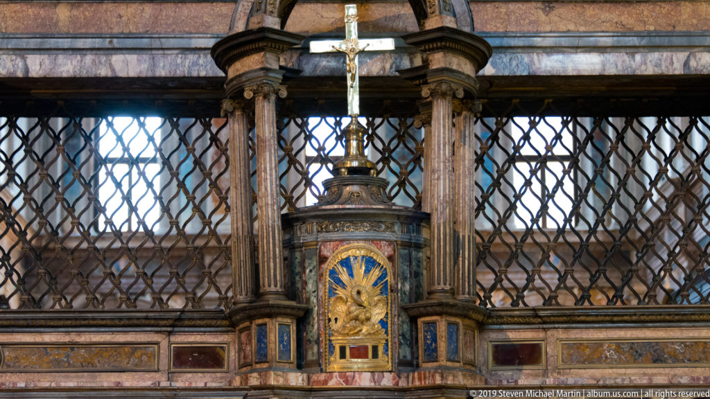Ornate dark wood and gilded tabernacle-like structure set against a metal grille on the church partition.