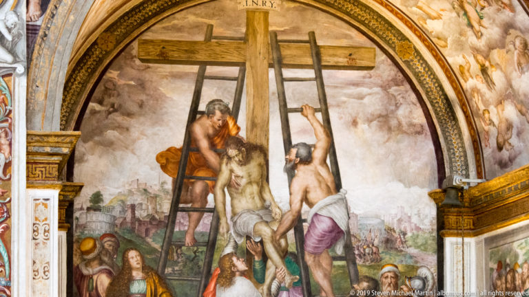 Deposition fresco with men lowering Christ from the central cross using ladders, mourners below, and two other crosses behind.