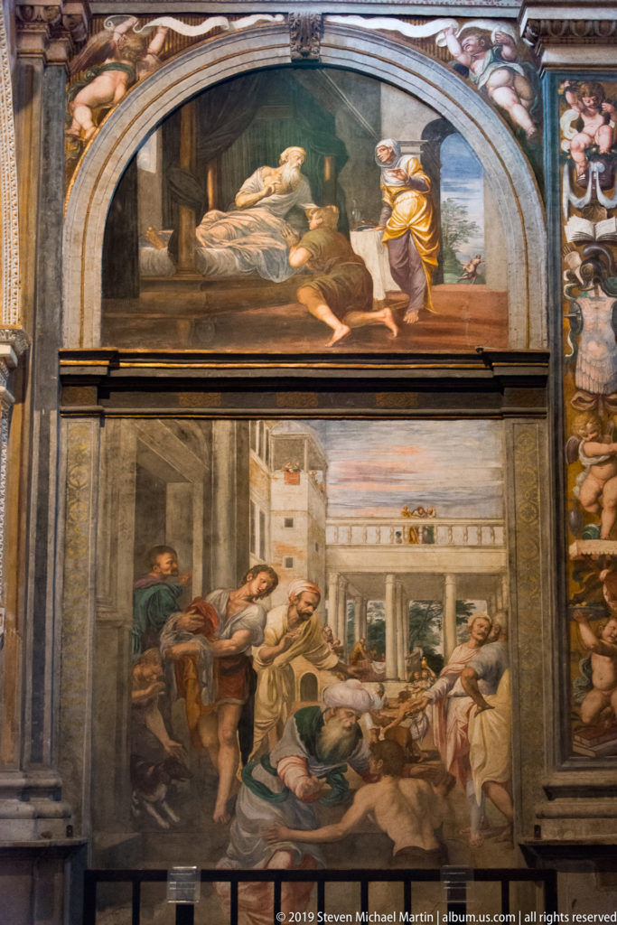 Arched wall bay containing two stacked Renaissance fresco scenes, a bedchamber above and a crowded courtyard narrative below.