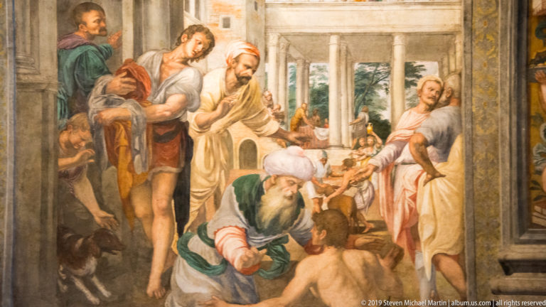 Renaissance fresco of men gathered around a crouching figure in a columned courtyard, with hands extended toward the central action.