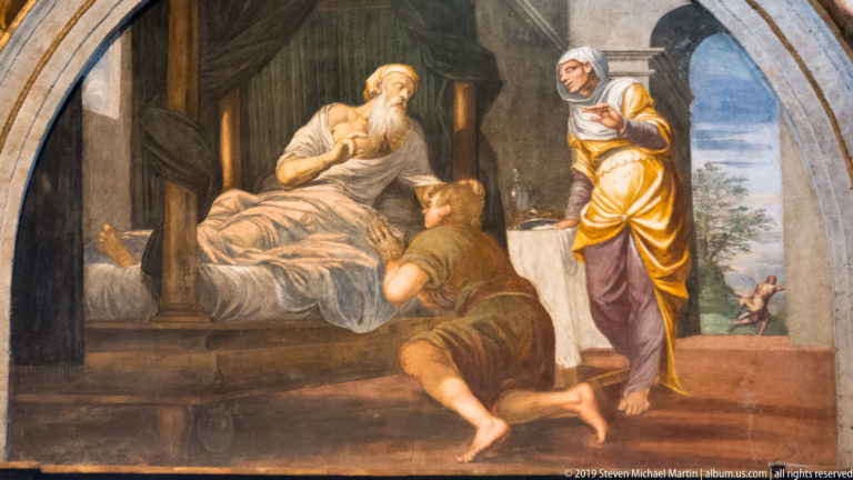 Fresco of an elderly bearded man in bed with two attendants, inside a room opening through an arch to a landscape.