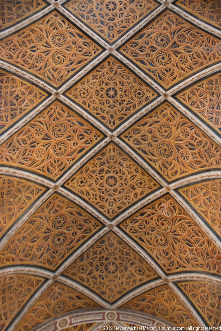 Close detail of a geometric coffered ceiling filled with repeating diamond panels and scrolling vegetal ornament.