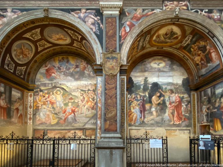Two large Renaissance fresco scenes beneath arches, separated by an ornate painted pier and fronted by a low metal rail.