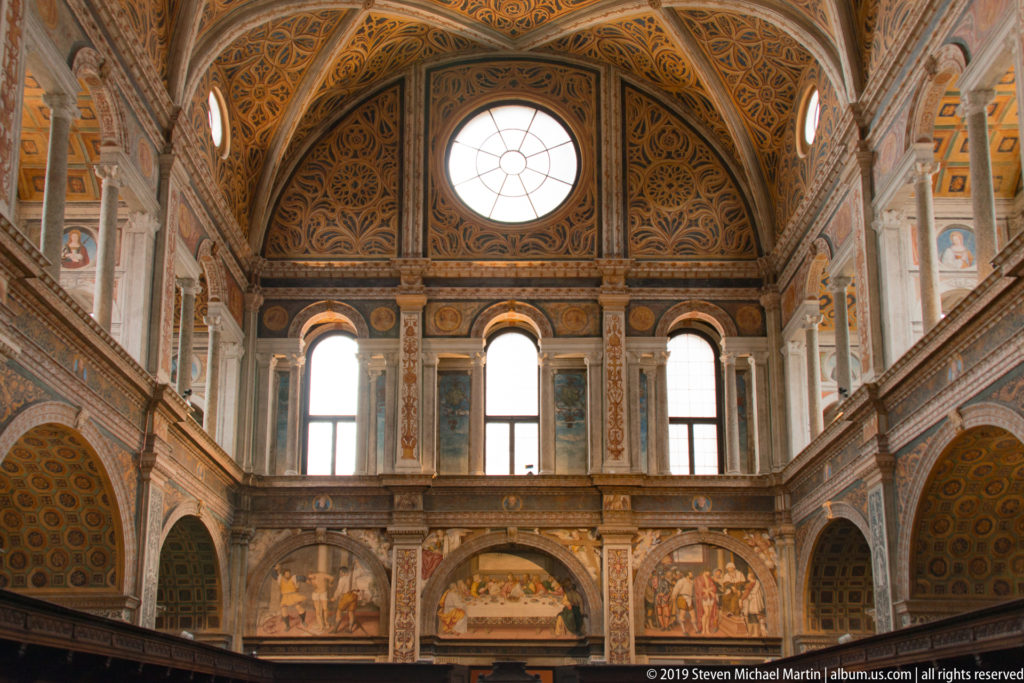 Upper gallery of San Maurizio with tall windows, fresco panels, painted pilasters, and an ornate coffered vault.