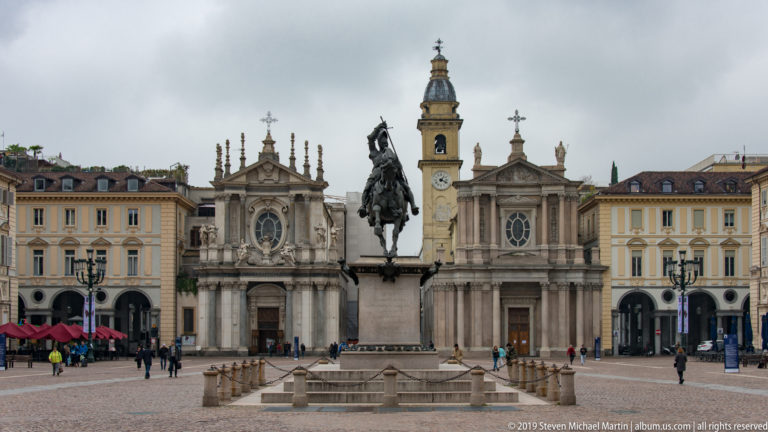 Frontal view of Piazza San Carlo’s twin churches and the equestrian statue of Emanuele Filiberto, with lamps and stonework in front.