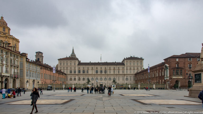 Wide view across Piazza Castello toward Palazzo Reale, with historic buildings and pedestrians lining the square.