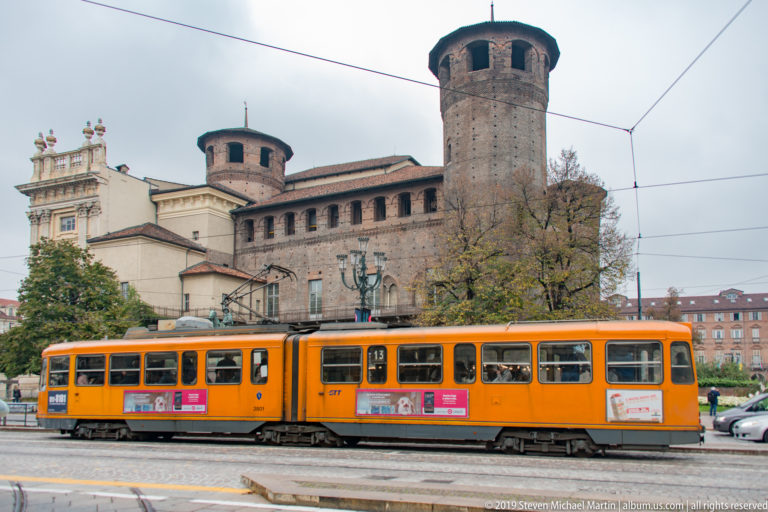 Orange tram passing the round brick towers and medieval rear section of Palazzo Madama in Turin.