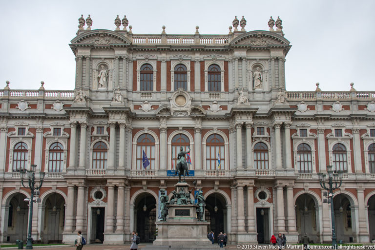 Ornate Palazzo Madama façade with arcades and flags behind an equestrian monument in Piazza Castello.