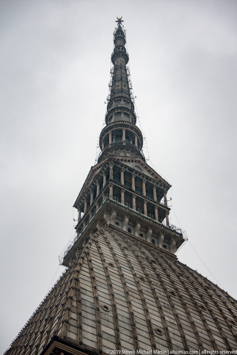 Close view of the Mole Antonelliana roof ribs and stacked upper tower stages against a gray sky.