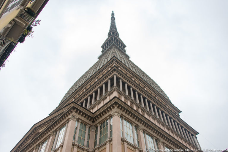 Upward corner view of the Mole Antonelliana, with stacked galleries narrowing into its tall spire.