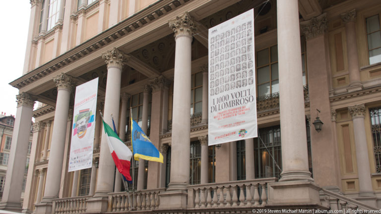 Tall classical columns, exhibition banners, and Italian and European flags on a monumental Turin public building.