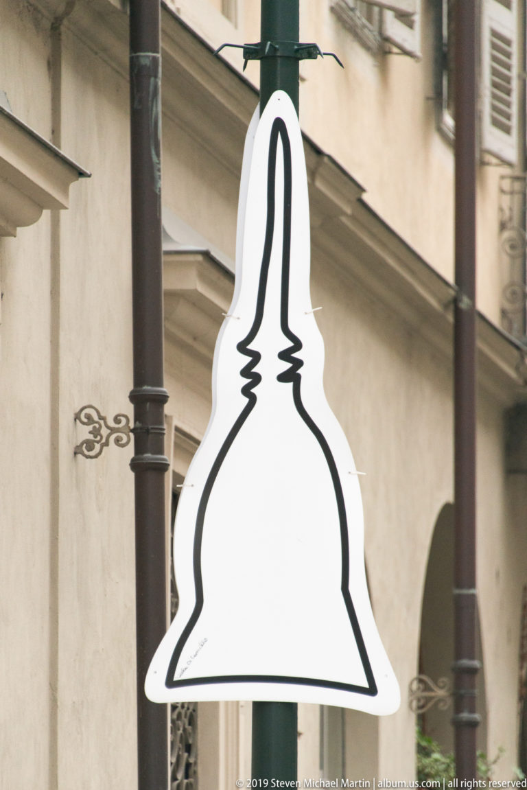 Black-and-white onion-dome silhouette mounted beside iron street lamps and a pale building façade in Turin.
