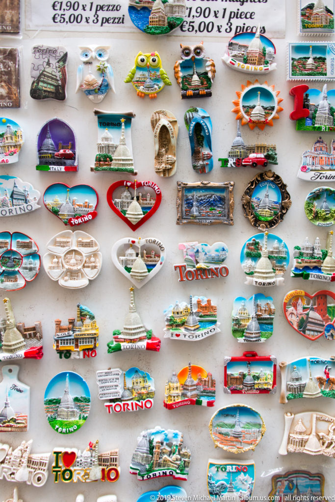 Display board packed with colorful Turin souvenir magnets featuring Torino lettering, miniature landmarks, and city motifs.