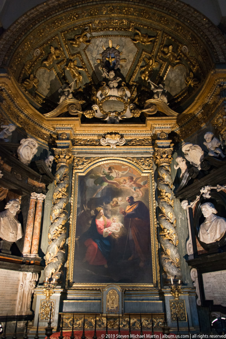 Closer frontal view of a religious altarpiece framed by spiral columns and multiple white portrait busts in a gilded chapel.