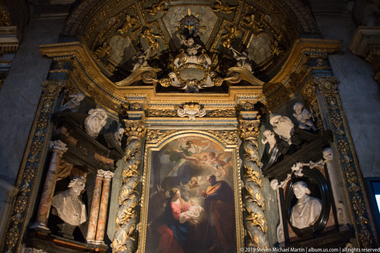 Richly ornamented chapel with a central religious painting surrounded by sculpted portrait busts, columns, and gilded carving.