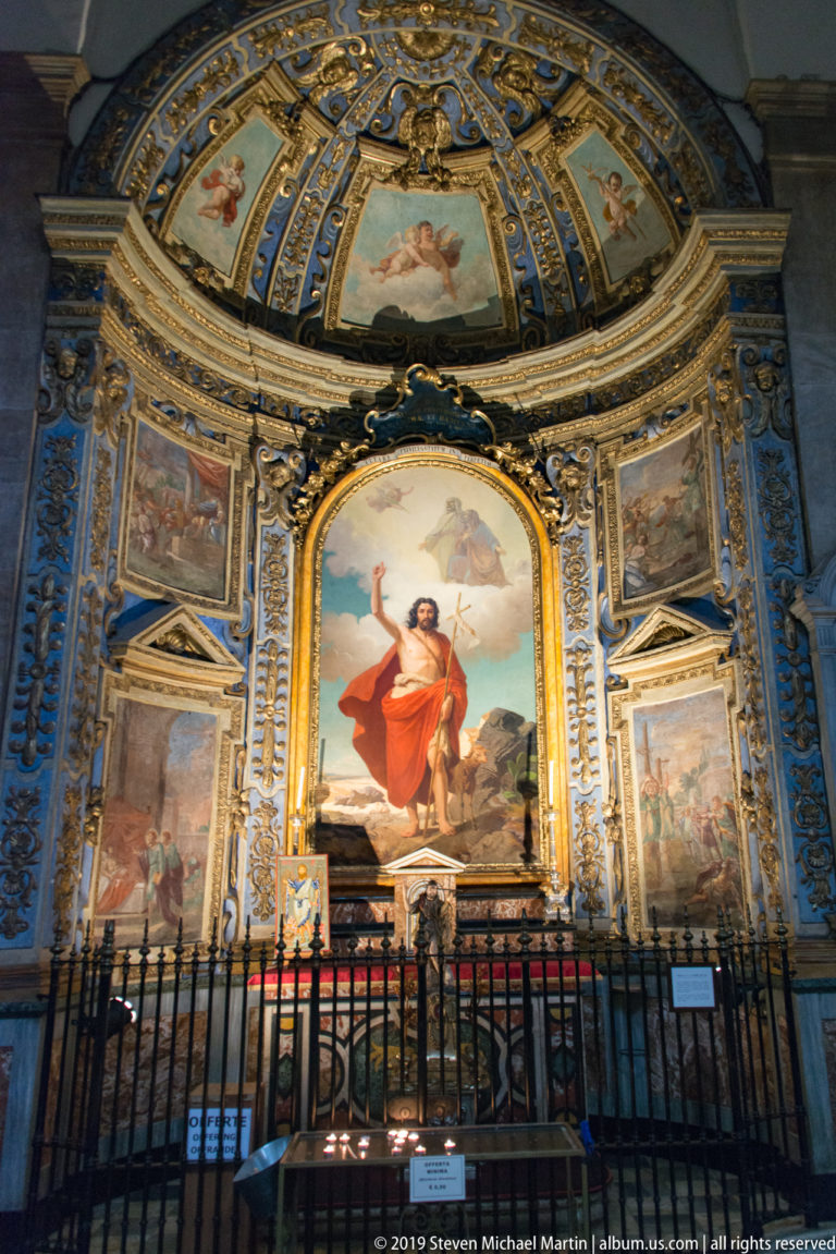 Ornate blue-and-gold chapel with a central painting of Saint John the Baptist, surrounding frescoes, and a metal screen.