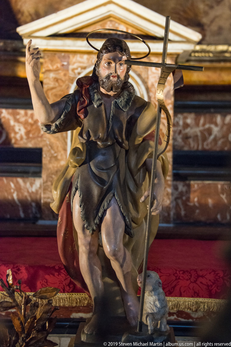 Polychrome statue of Saint John the Baptist holding a cross-staff, wearing a rough garment and mantle.