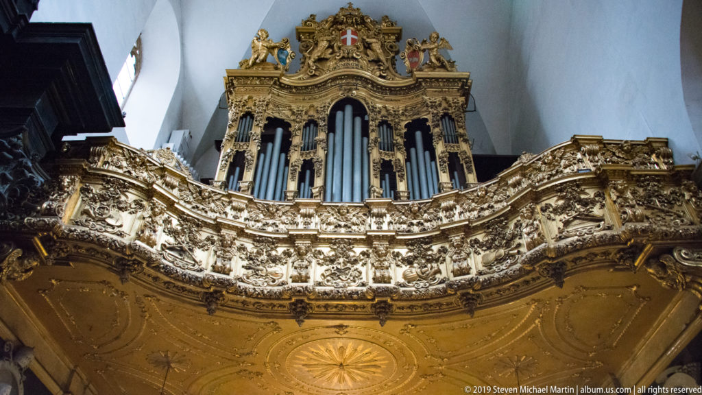 Ornate organ case with vertical pipes rising above a richly carved and gilded gallery inside Turin Cathedral.