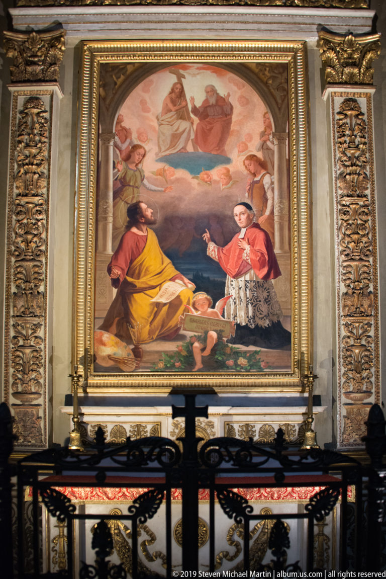 Large religious painting with a seated cleric and kneeling churchman above an altar behind an ornamental metal rail.