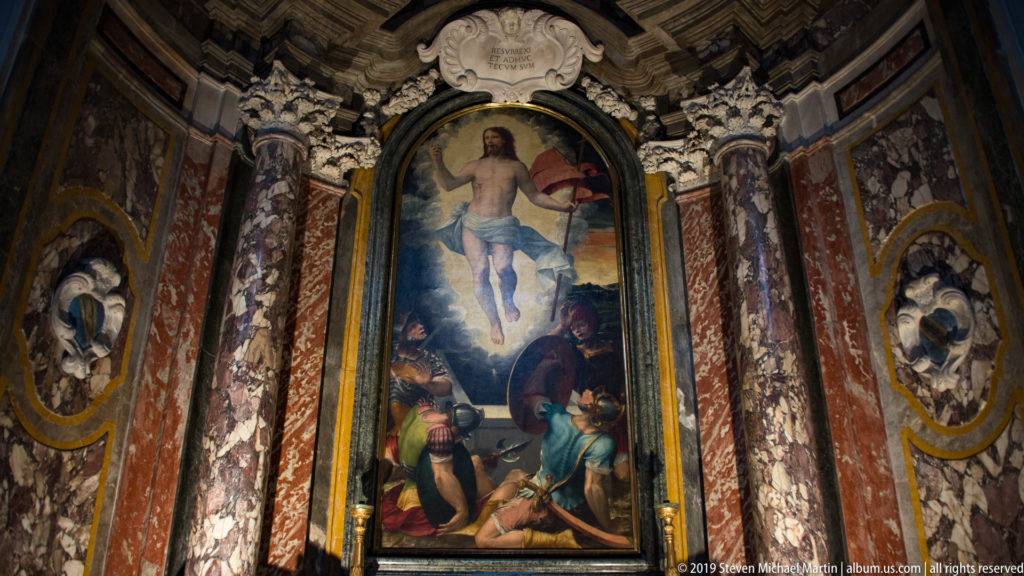 Painted risen Christ above figures at the tomb, framed by red marble columns and elaborate chapel ornament.