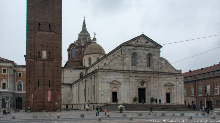 Front of Turin Cathedral with the brick bell tower at left and the ornate Shroud Chapel dome rising behind the roof.