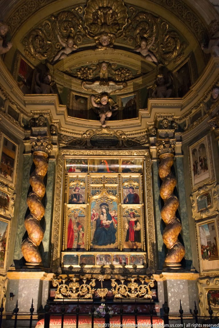Multi-panel painted altarpiece with a Madonna and Child at center, framed by spiral columns and elaborate gilded ornament.