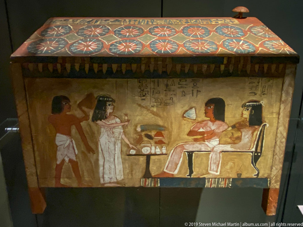 Painted Egyptian funerary chest with a pitched decorated lid, offering scene, seated figures, and hieroglyphic inscription.