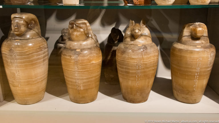 Four pale stone Egyptian canopic jars with human- and animal-headed lids and vertical hieroglyphic inscriptions.