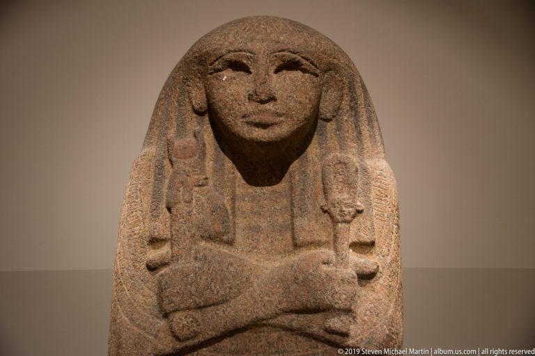 Granite anthropoid sarcophagus lid with idealized face, broad wig, and crossed arms over the chest.