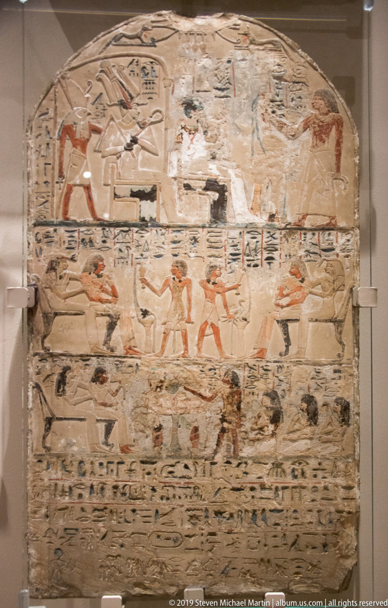 Rounded-top Egyptian painted stela with multiple registers of figures, animals, offerings, and hieroglyphic text.