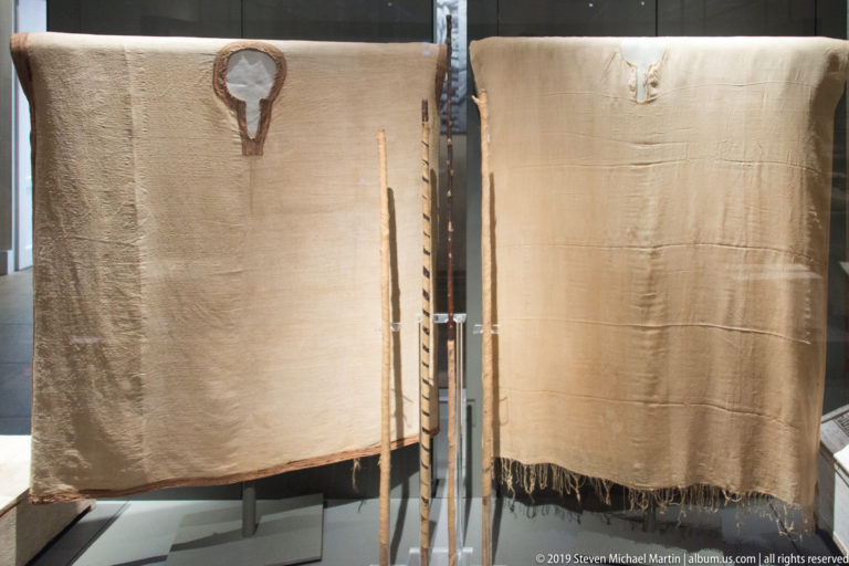 Large plain beige Egyptian textile hanging vertically, with worn edges and a second textile panel displayed beside it.