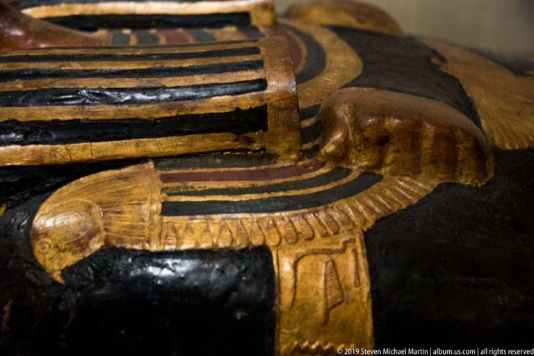 Close detail of a gilded falcon with spread wings on a black-and-gold decorated Egyptian coffin.