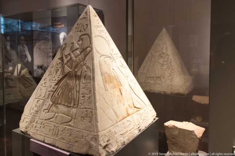 Four-sided Egyptian pyramidion carved with a worship scene, divine figure, and vertical hieroglyphic inscriptions.