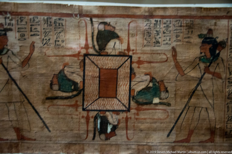 Painted Egyptian funerary textile with a central rectangle, surrounding deities, red lines, and hieroglyphic groups above.