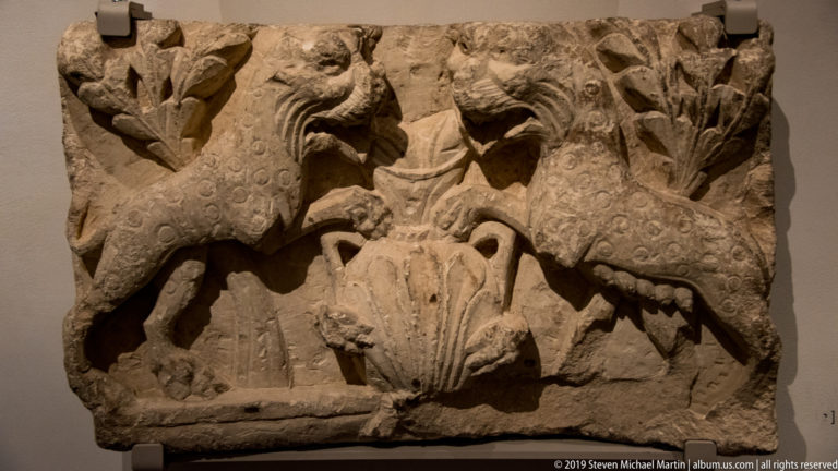 Stone relief with two opposed winged, spotted creatures flanking a central carved motif.