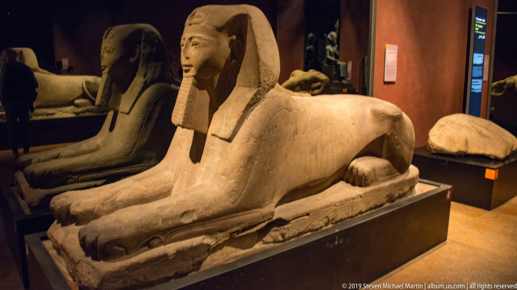 Large recumbent Egyptian sphinx with royal head, nemes headdress, extended forepaws, and lion body on a stone plinth.