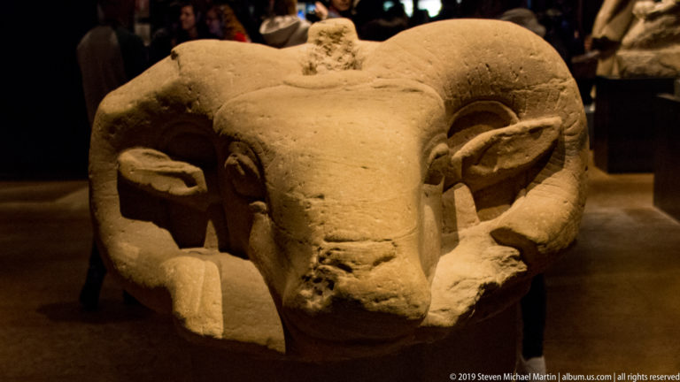 Frontal sandstone head of an Amun criosphinx with massive curling horns, broad forehead, and projecting muzzle.
