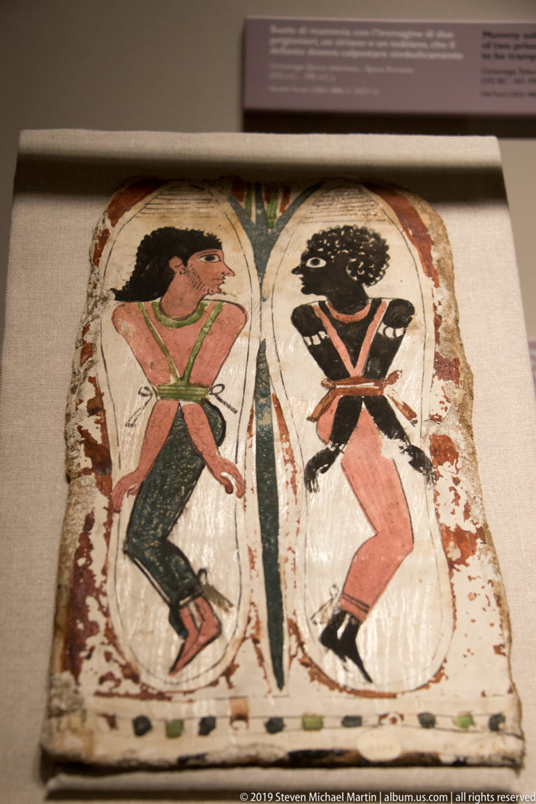 Painted Egyptian funerary panel with two crouching male figures facing opposite directions on either side of a central motif.