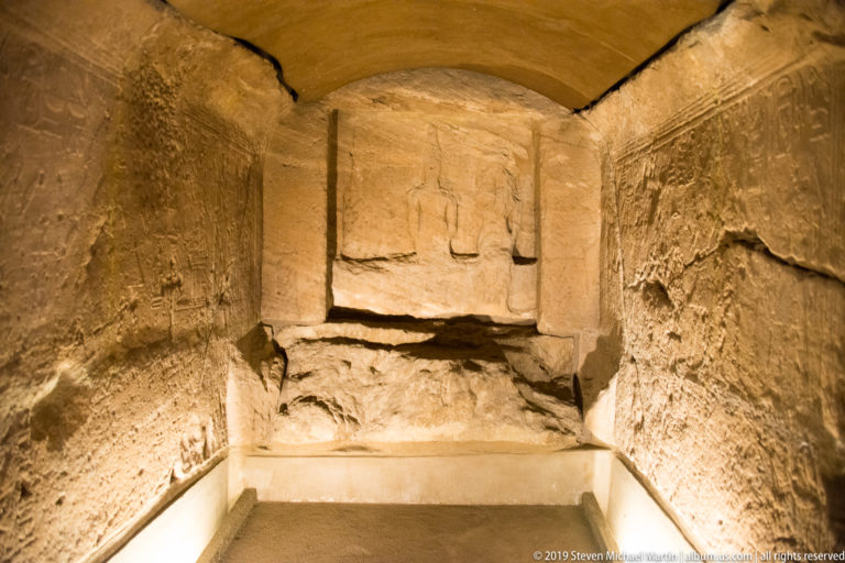 Interior of the sandstone rock-cut chapel of Ellesiya, with incised wall reliefs and standing figures in the rear sanctuary.