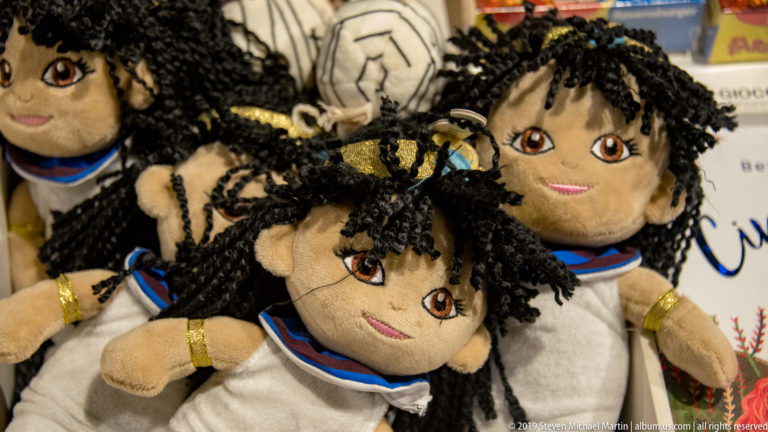 Cluster of plush Egyptian-themed dolls with dark yarn hair, white clothing, colored collars, and gold-toned armbands.