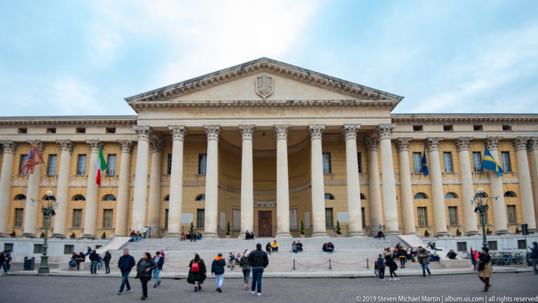 Palazzo Barbieri in Piazza Bra with tall neoclassical colonnade, triangular pediment, symmetrical wings, and civic flags.