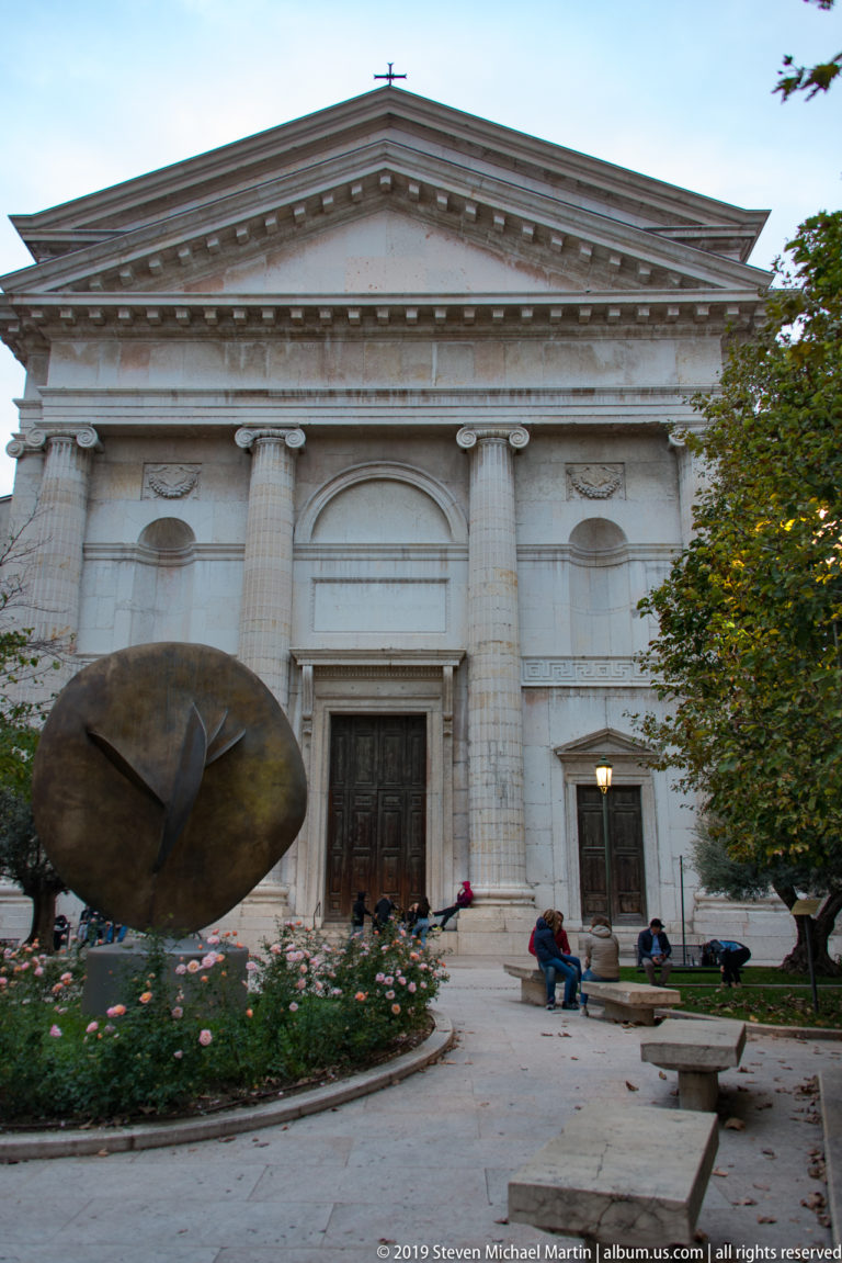 San Nicolò all’Arena façade with four giant columns and triangular pediment behind a large dark circular sculpture.