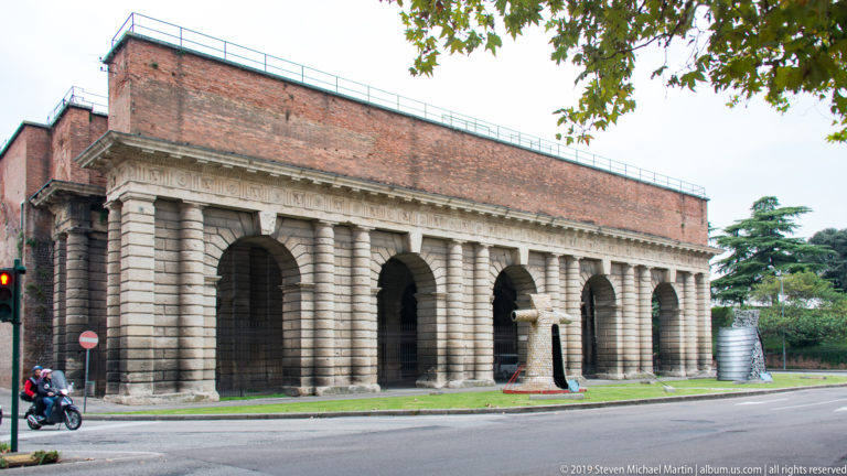 Long side elevation of Porta Nuova with repeated deep arches, rusticated piers, red-tiled roof, and roadway in front.