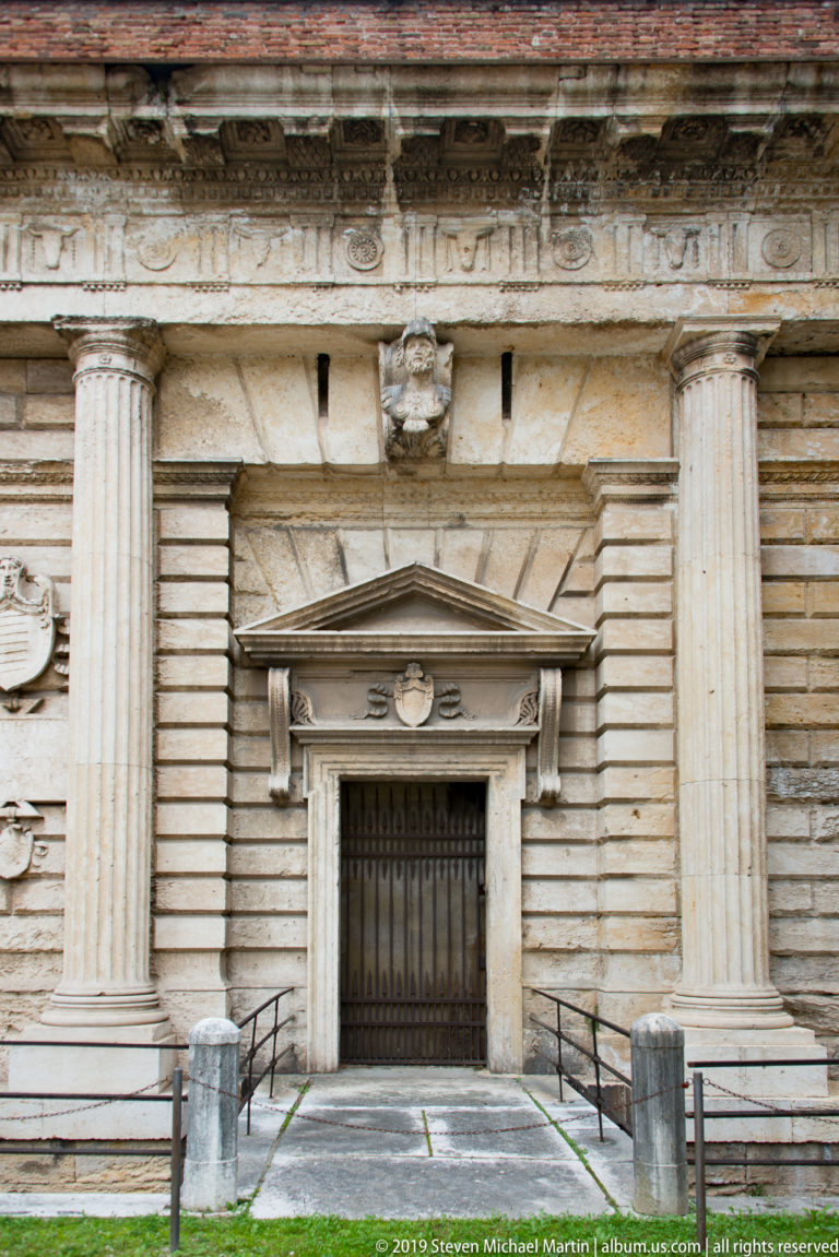 Secondary Porta Nuova doorway with triangular pediment, iron gate, rusticated masonry, and fluted columns.