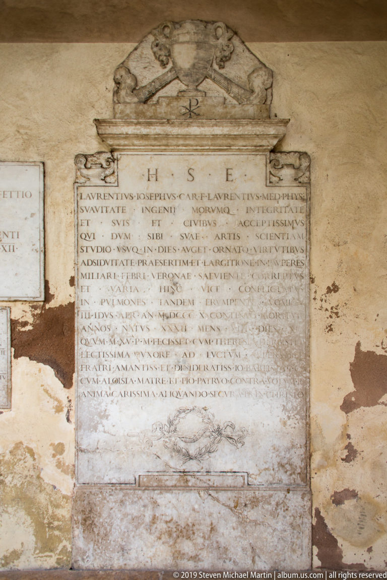 Large Latin-inscribed marble plaque beneath a carved portrait relief on a worn plaster wall.