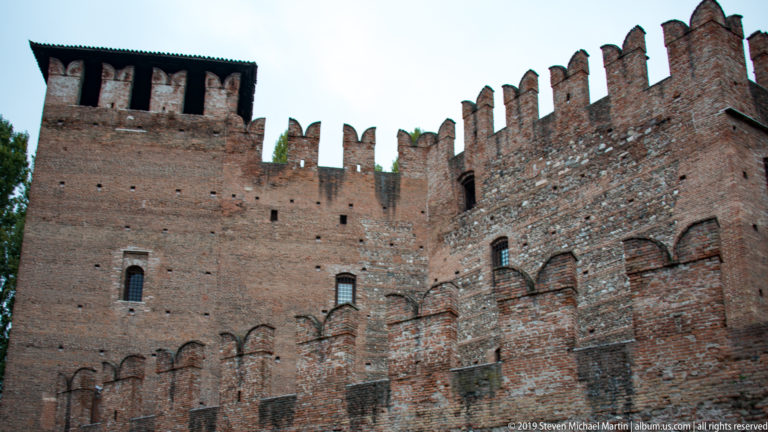 Close upward view of Castelvecchio brick walls and towers crowned with repeated swallowtail crenellations.