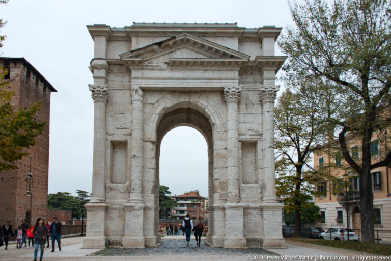 Freestanding Arco dei Gavi with tall central arch, classical columns, pediment, and pedestrians passing beneath.