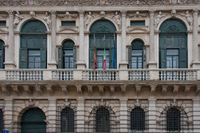 Palazzo Canossa façade with rusticated ground floor, tall windows, paired columns, balustrade, flags, and sculptural ornament.