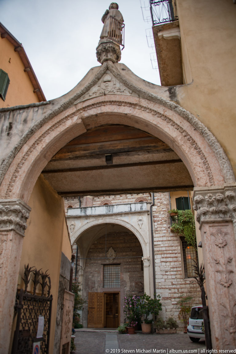 Stone gateway framing a second pointed-arch entrance with striped masonry and a wooden door beyond.