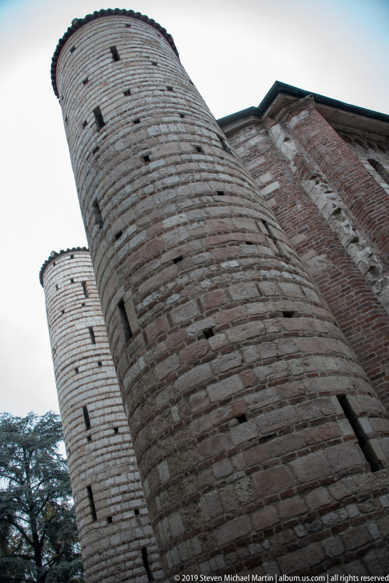 Two cylindrical stone towers of San Lorenzo viewed from below beside adjoining brick church walls.